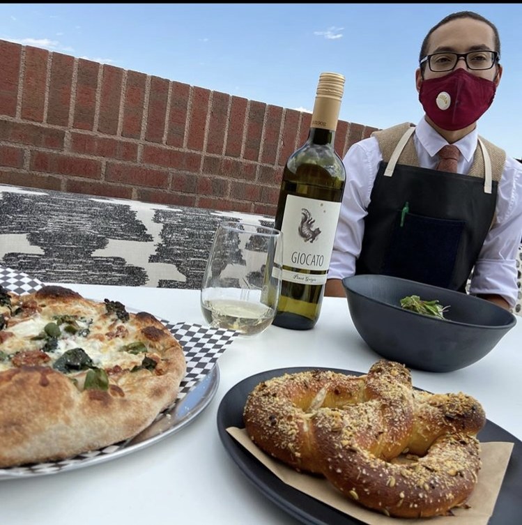Christopher Stotts serving pizza, a pretzel and wine on a Boulder rooftop patio